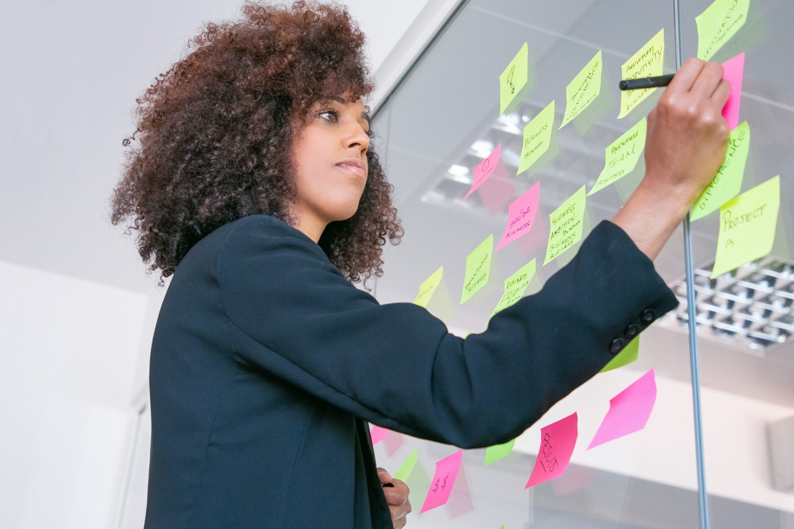 Successful pretty businesswoman writing on sticker with marker. Thoughtful confident curly female manager sharing idea for project and making note. Brainstorming, business and training concept